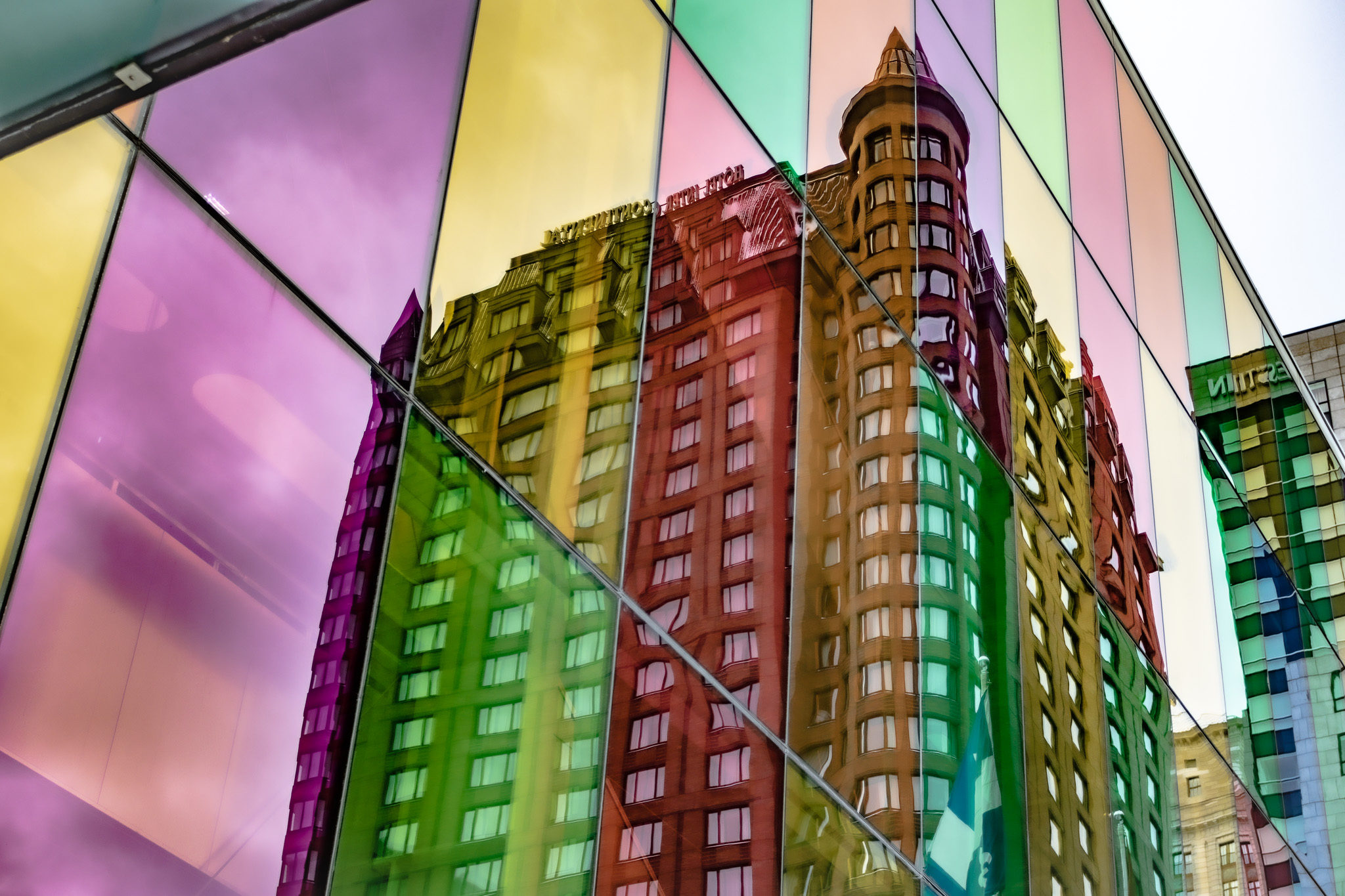 The reflection of a building seen through a set of rainbow glass windows